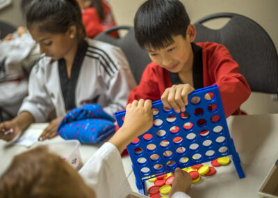 Children at a table playing a blue vertical Connect Four-style game with red and yellow discs. (informative)