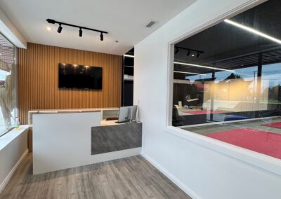 Reception area with white curved desk, wooden slat accent wall, and a mounted flat-screen TV.